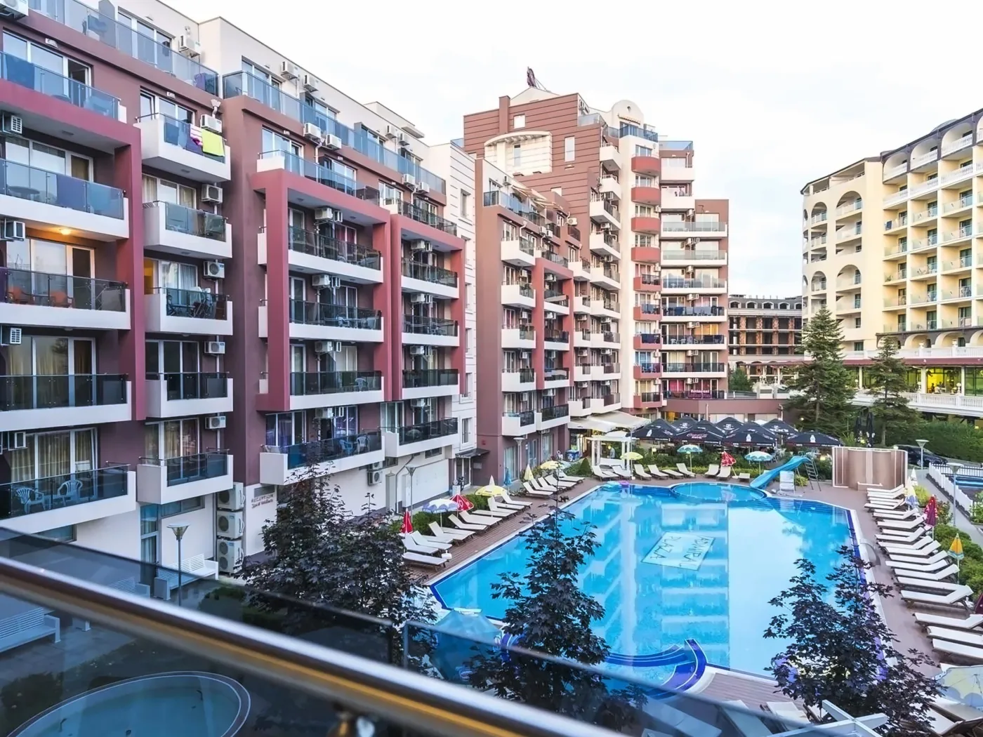 Vedere a piscinei hotelului înconjurată de clădiri și șezlonguri. - Vedere a piscinei hotelului înconjurată de clădiri și șezlonguri.