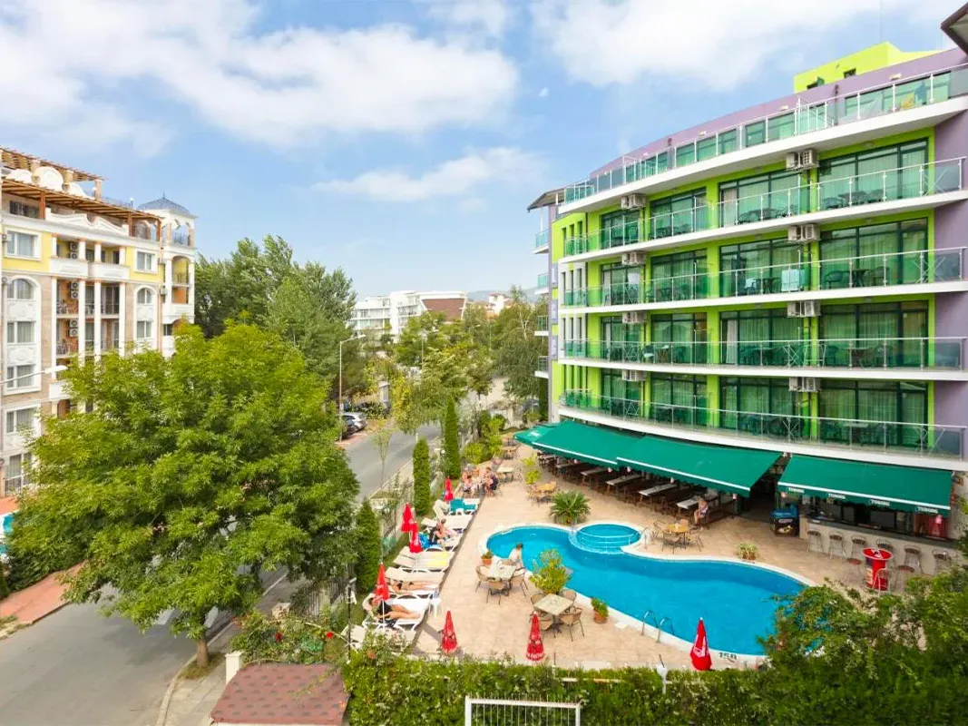 Vedere a zonei piscinei hotelului cu clădiri verzi și șezlonguri. - Vedere a zonei piscinei hotelului cu clădiri verzi și șezlonguri.