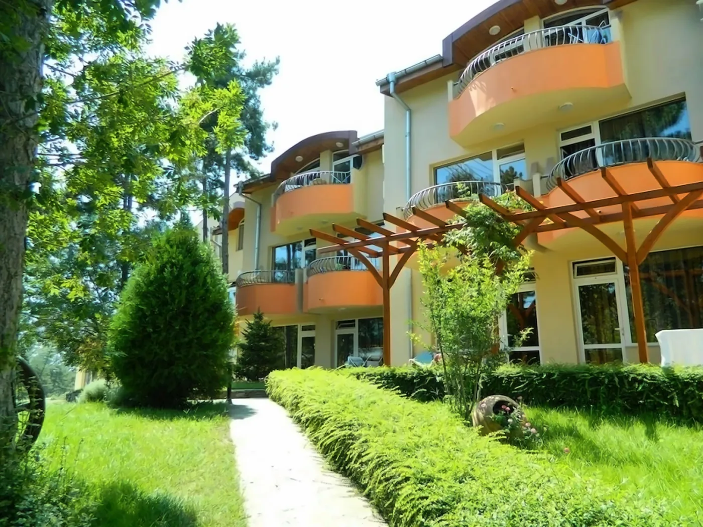 Vedere exterioară a hotelului cu balcoane portocalii și peisaj verde. - Vedere exterioară a hotelului cu balcoane portocalii și peisaj verde.