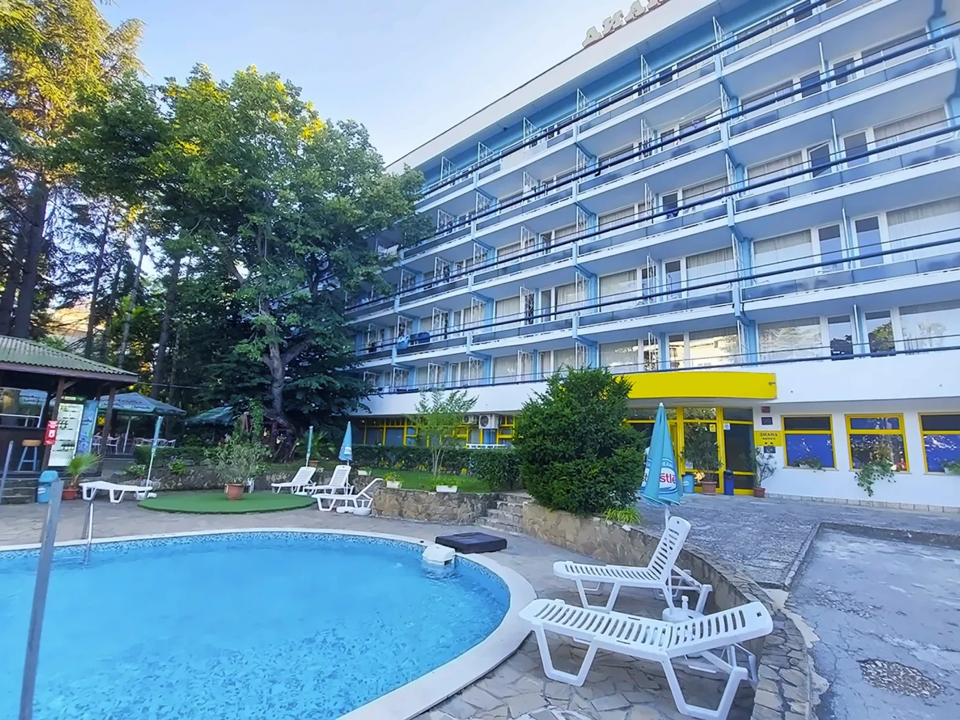 Clădirea hotelului cu zonă de piscină, șezlonguri și copaci în fundal. - Clădirea hotelului cu zonă de piscină, șezlonguri și copaci în fundal.